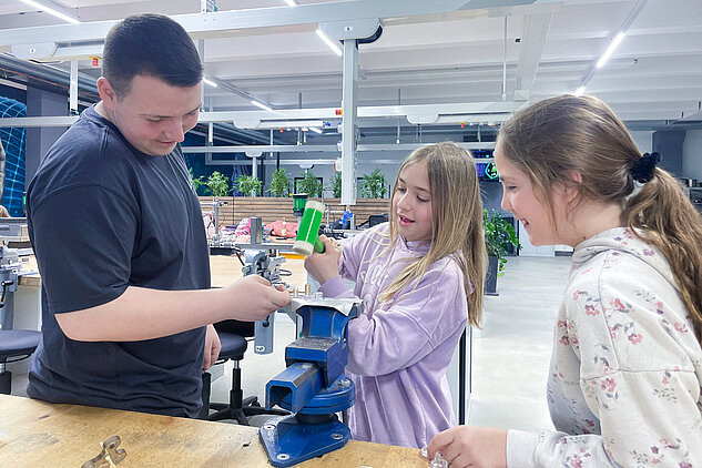 Two girls practicing with different tools, supported by an apprentice