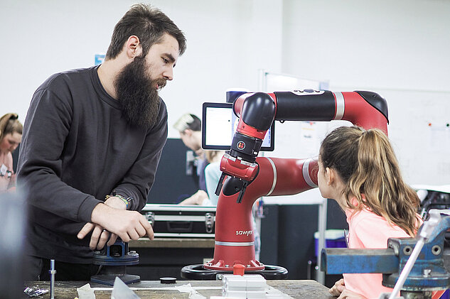 Ein Auszubildender erklärt einem jungen Mädchen den Roboter Sawyer